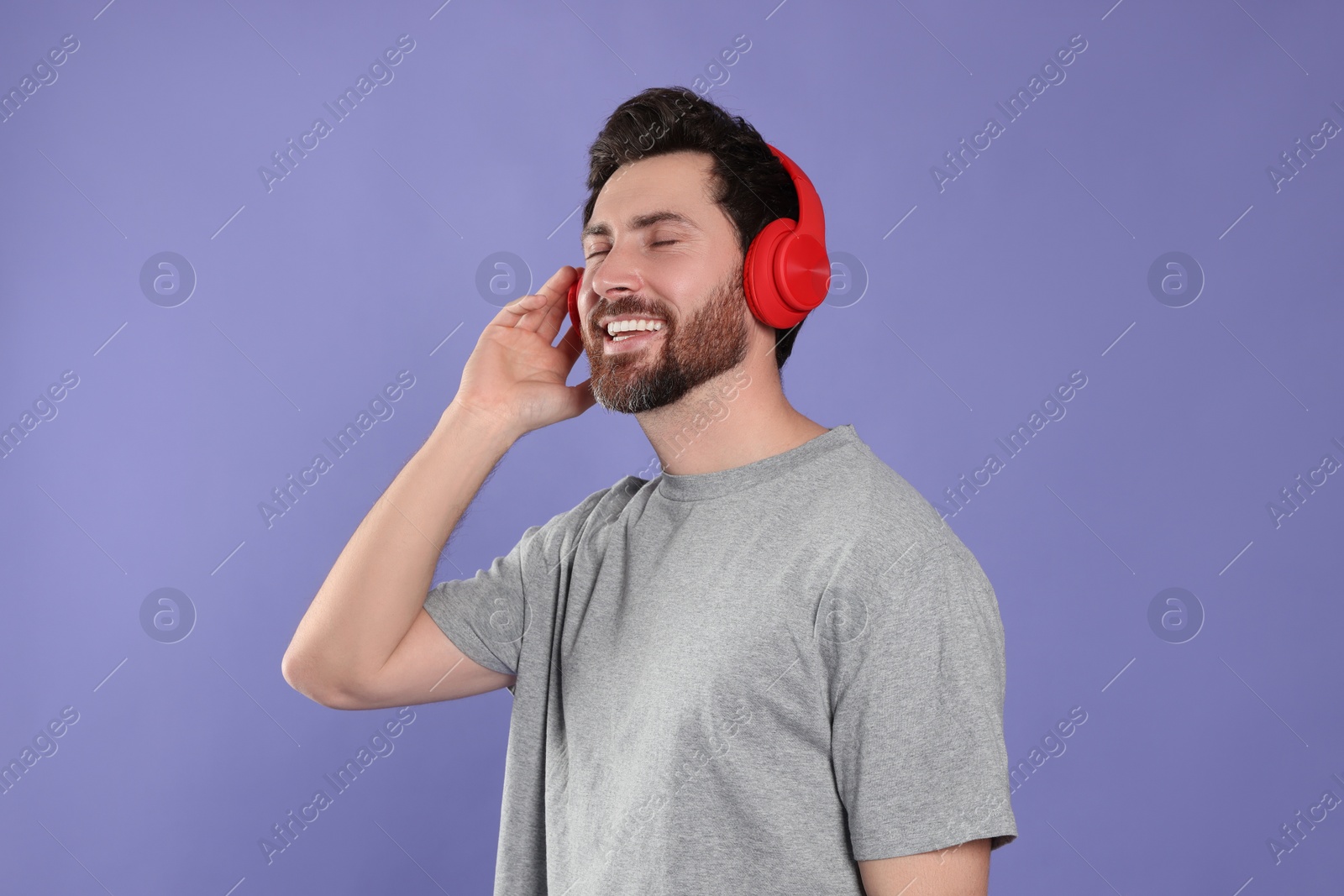 Photo of Happy man listening music with headphones on violet background