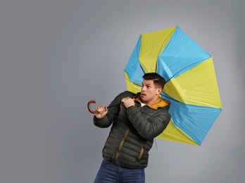 Emotional man with umbrella caught in gust of wind on grey background