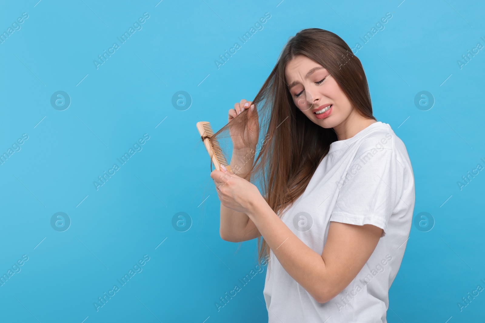 Photo of Upset woman brushing her hair on light blue background, space for text. Alopecia problem