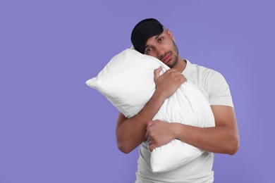 Photo of Tired man with pillow and sleep mask on violet background, space for text. Insomnia problem