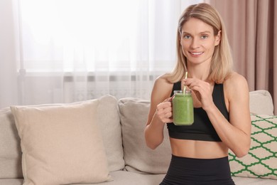 Photo of Young woman in sportswear with mason jar of fresh smoothie at home, space for text