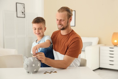 Father and son putting coin into piggy bank at home