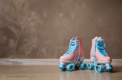 Vintage roller skates on floor near brown wall. Space for text