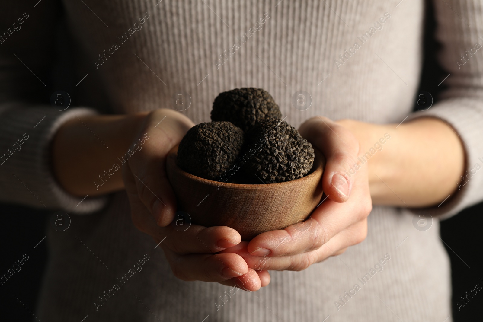 Photo of Woman holding wooden bowl of black truffles in hands, closeup