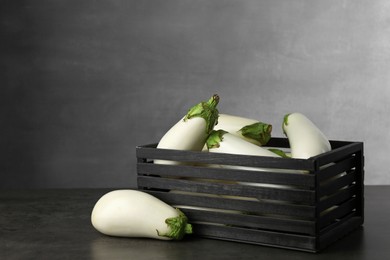 Wooden crate with white eggplants on black textured table against grey background