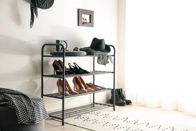 Photo of Black shelving unit with shoes and different accessories near white wall in hall