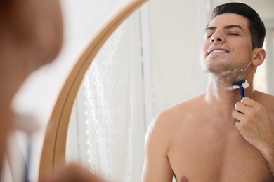 Handsome man shaving near mirror in bathroom