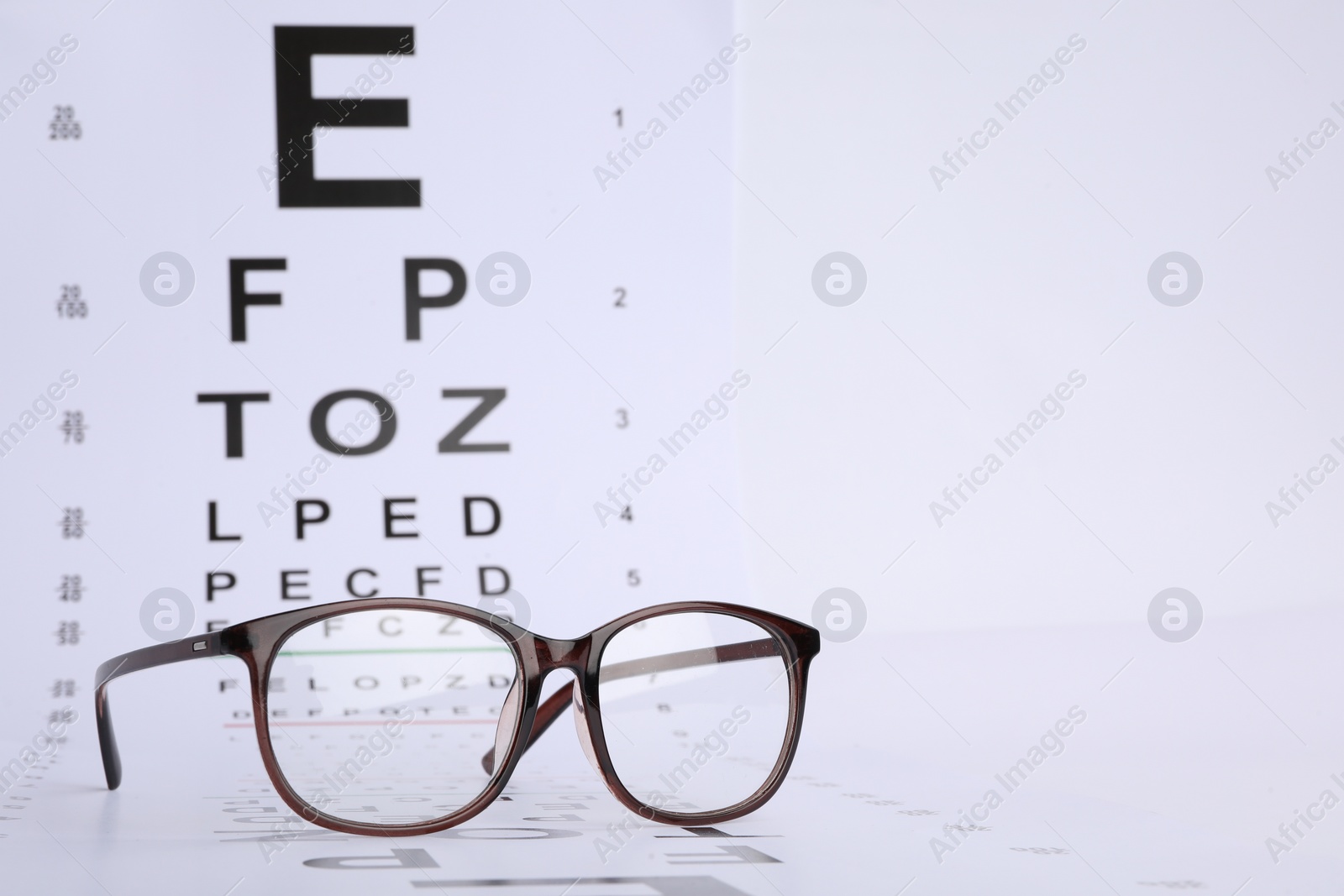 Photo of Vision test chart and glasses on white background, closeup. Space for text