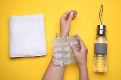Woman with ice pack, bottle of water and towel on yellow background, top view. Heat stroke treatment