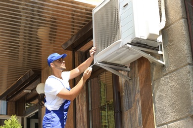 Photo of Professional technician maintaining modern air conditioner outdoors