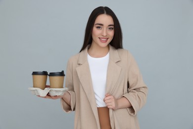 Photo of Young female intern holding takeaway cardboard cups on grey background