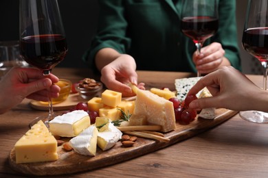 Photo of Women with cheese plate and glasses of wine at wooden table, closeup