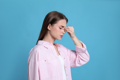 Photo of Young woman suffering from headache on light blue background