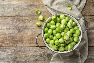 Photo of Colander with Brussels sprouts and cloth on wooden background, top view. Space for text