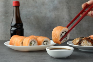 Photo of Woman dipping tasty sushi roll with salmon into soy sauce at grey table, closeup