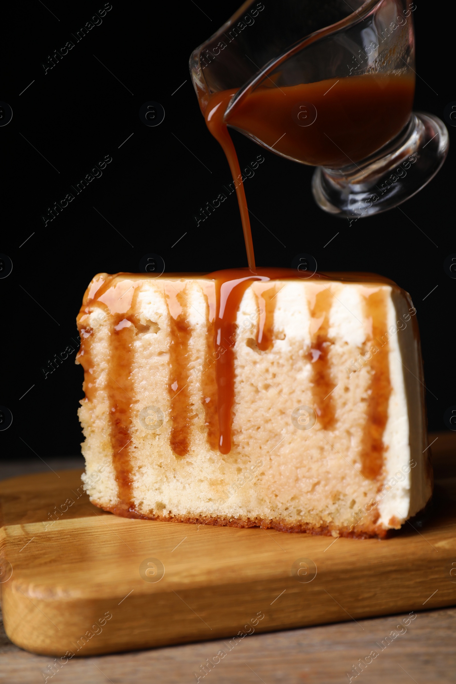 Photo of Pouring caramel sauce on slice of cake at wooden table