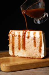 Photo of Pouring caramel sauce on slice of cake at wooden table