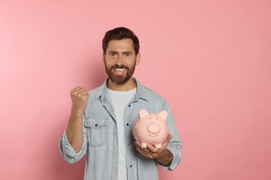 Photo of Happy man with ceramic piggy bank on pale pink background