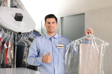 Photo of Portrait of happy worker with clothes near counter at dry-cleaner's