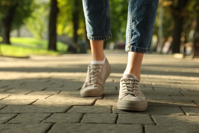 Photo of Woman in stylish sneakers walking on city street, closeup. Space for text