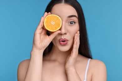 Emotional young woman with piece of orange on light blue background