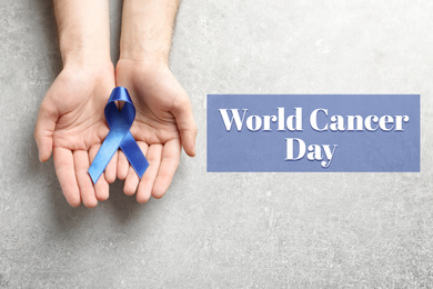 Man holding blue ribbon on grey background, top view. World Cancer Day