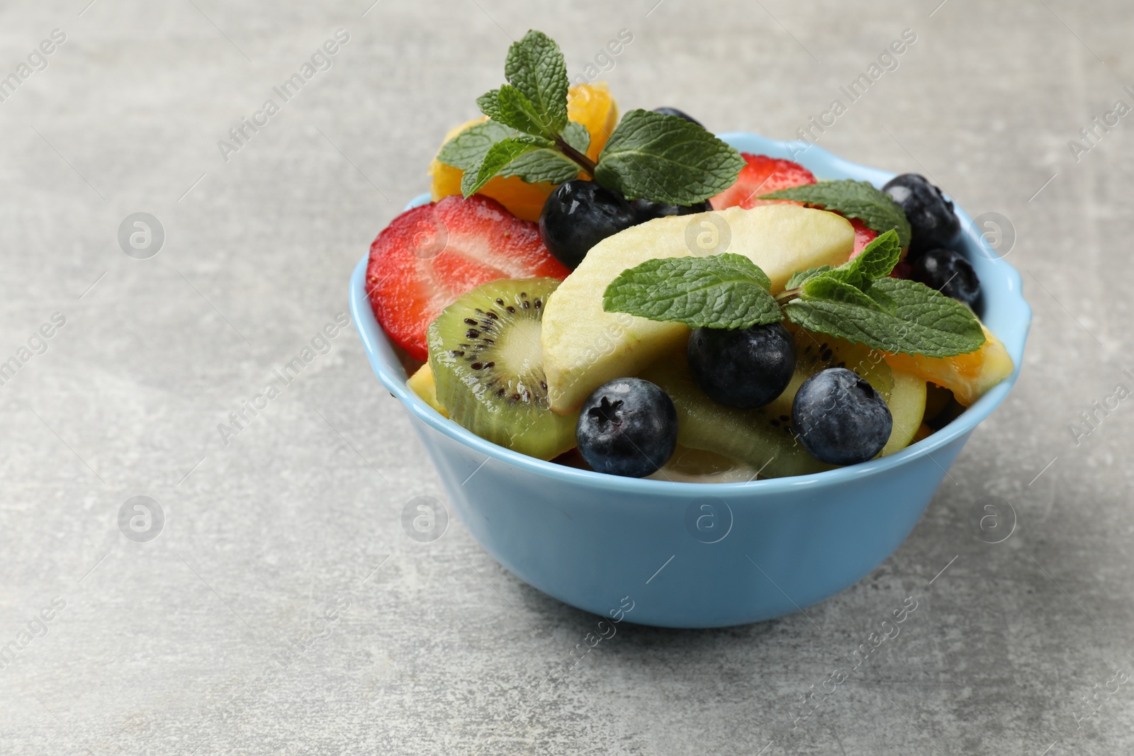 Photo of Tasty fruit salad in bowl on gray textured table, closeup. Space for text