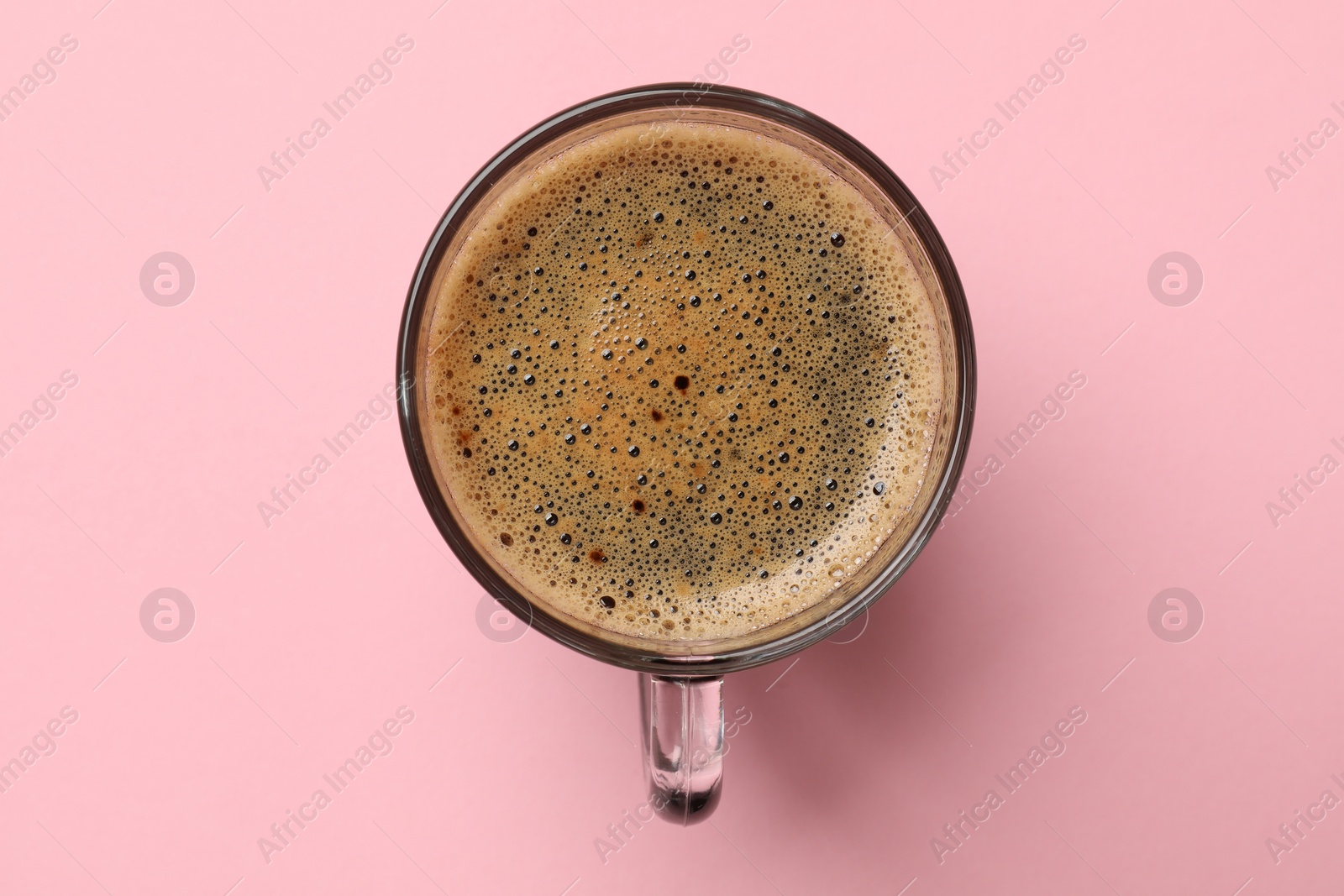 Photo of Aromatic coffee in glass cup on pink background, top view