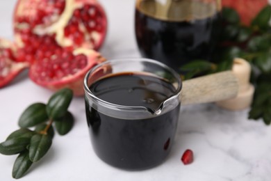 Photo of Tasty pomegranate sauce and branch on white marble table, closeup