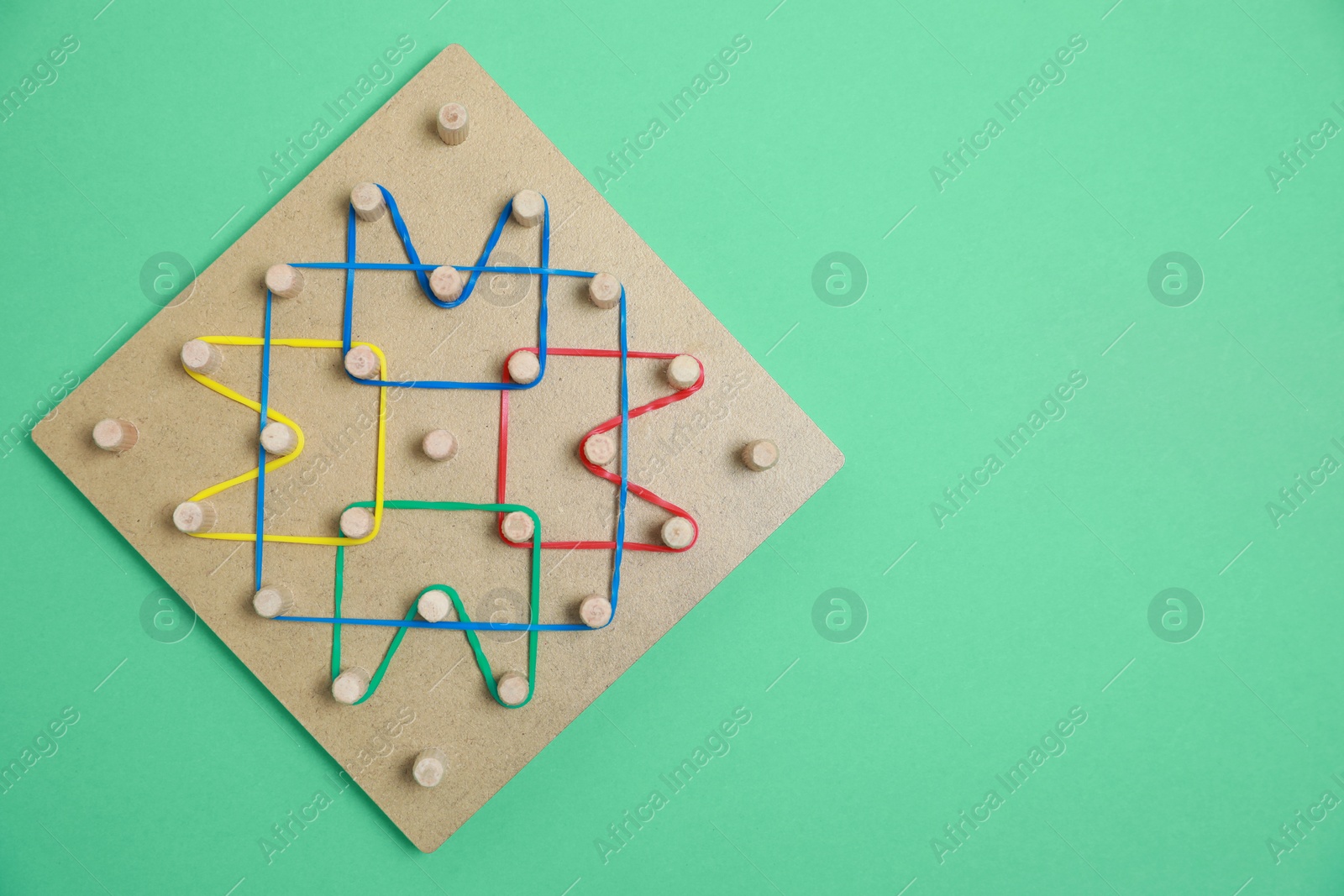 Photo of Wooden geoboard with rubber bands on green background, top view with space for text. Educational toy for motor skills development