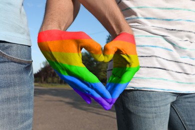 Image of Gay couple forming heart with hands in park, closeup