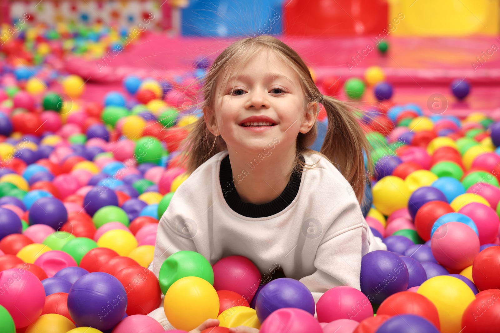 Photo of Happy little girl lying on colorful balls in ball pit