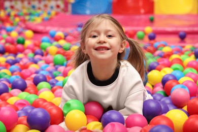 Photo of Happy little girl lying on colorful balls in ball pit