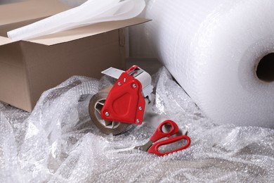 Photo of Adhesive tape with bubble wrap, scissors and cardboard box on table