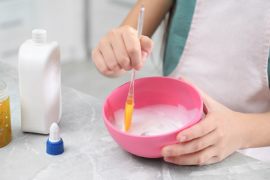 Little girl mixing ingredients with silicone spatula at table, closeup. DIY slime toy