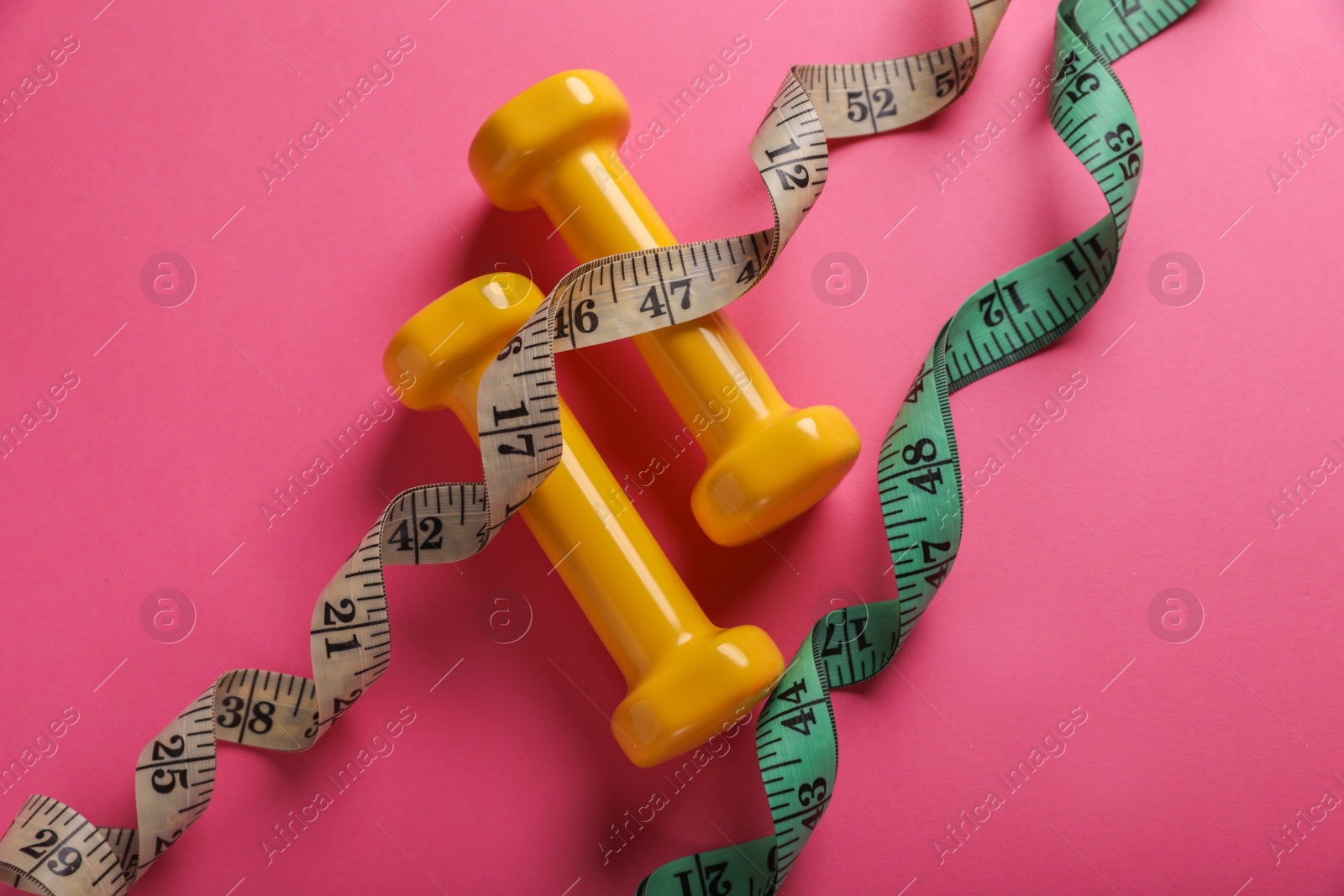 Photo of Measuring tapes and dumbbells on pink background, flat lay. Weight control concept