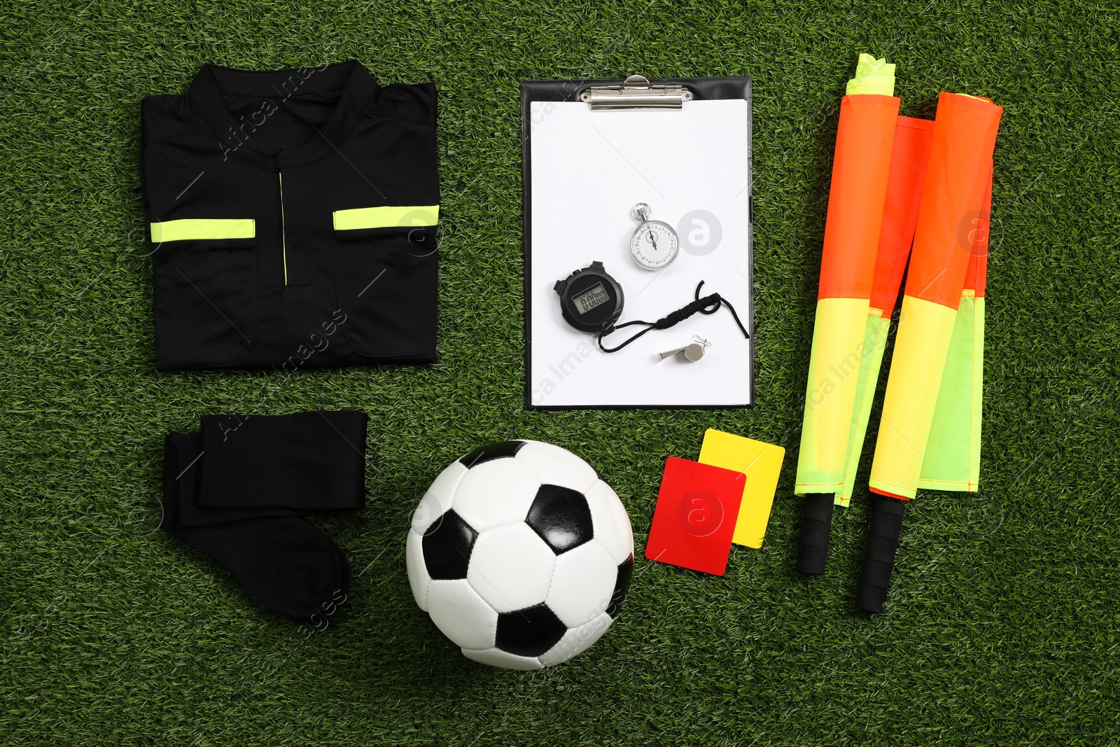 Photo of Uniform, soccer ball and other referee equipment on green grass, flat lay