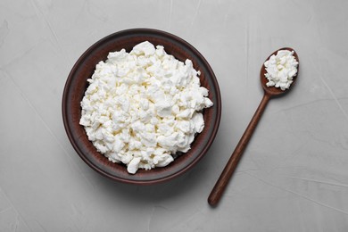 Photo of Clay bowl and spoon with cottage cheese on grey table, flat lay