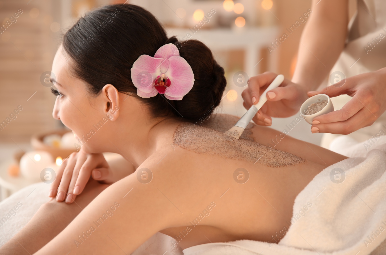 Photo of Beautiful young woman having massage with body scrub in spa salon