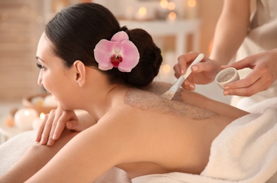 Beautiful young woman having massage with body scrub in spa salon