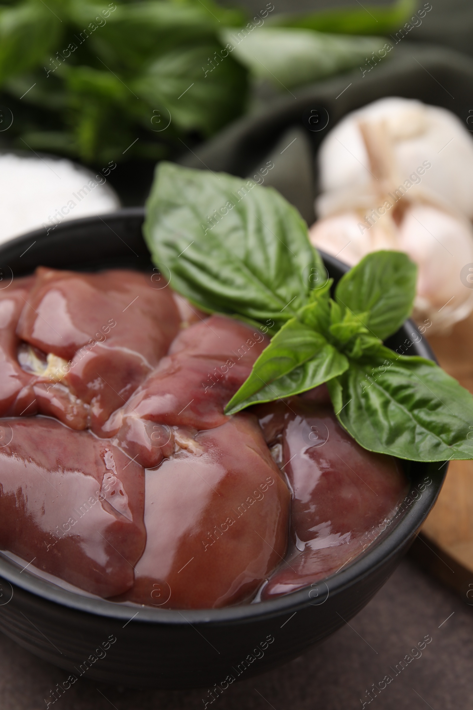 Photo of Bowl of raw chicken liver with basil on grey table, closeup