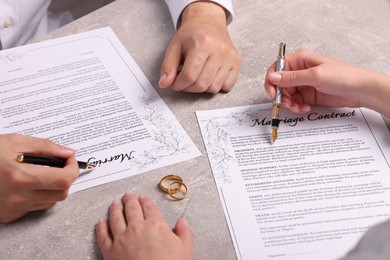 Man and woman signing marriage contract at light grey table, closeup