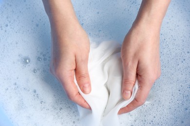 Photo of Top view of woman hand washing white clothing in suds, closeup