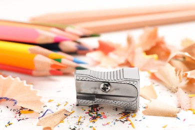 Photo of Sharpener, colorful pencils and shavings on white wooden table, closeup