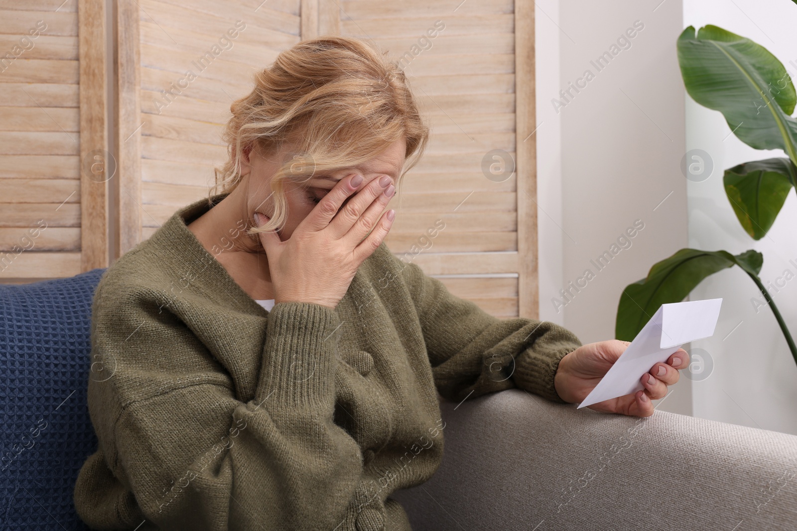 Photo of Upset middle aged woman with envelope on sofa at home. Loneliness concept