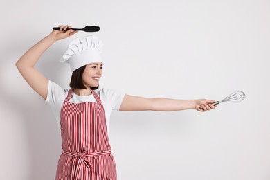 Happy confectioner with whisk and spatula on light grey background