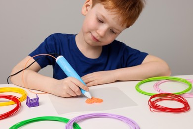 Photo of Boy drawing with stylish 3D pen at white table