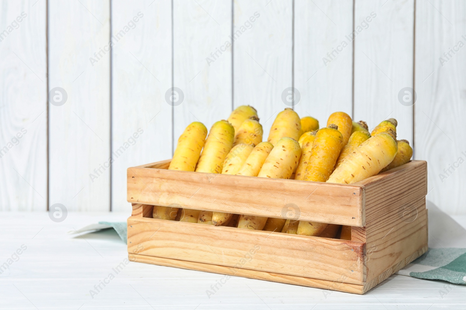 Photo of Many raw white and yellow carrots in wooden crate on table