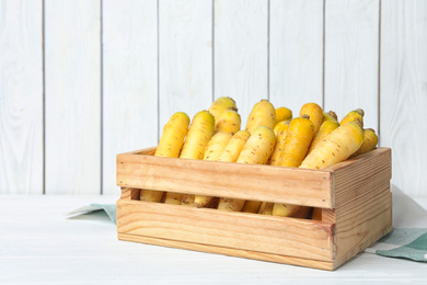 Photo of Many raw white and yellow carrots in wooden crate on table