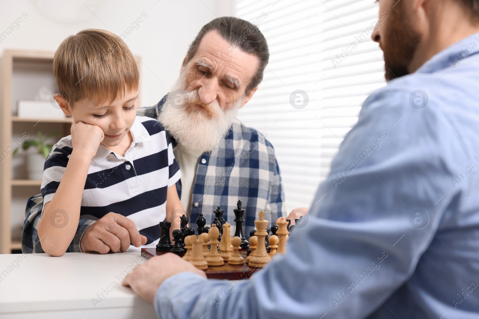 Photo of Family playing chess together at table in room